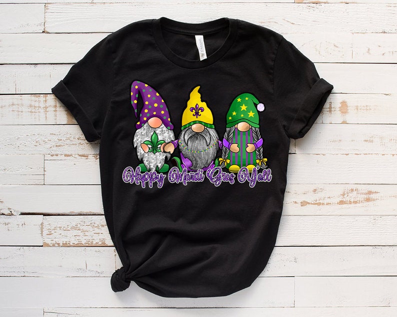 May include: Black t-shirt with a graphic of three gnomes wearing Mardi Gras colors and hats. The text "Happy Mardi Gras Y'all" is below the gnomes.