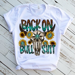 May include: White t-shirt with a turquoise and brown bull skull graphic and the text "Back on Bull Shit" with sunflowers around the skull.