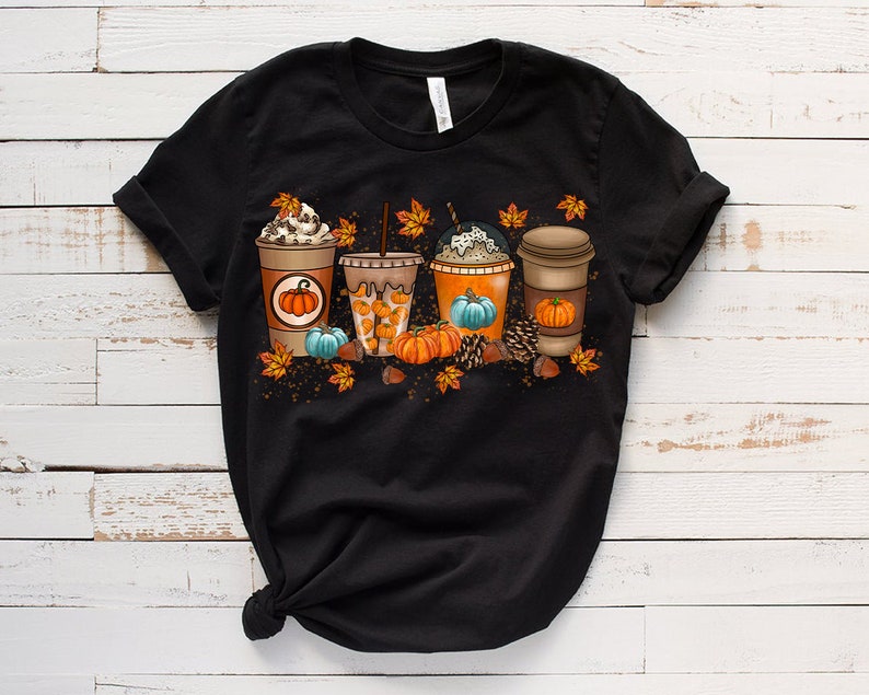 K&ouml;nnte beinhalten: Schwarzes T-Shirt mit einem Aufdruck von vier Herbst-Kaffeegetr&auml;nken mit K&uuml;rbissen und Bl&auml;ttern.