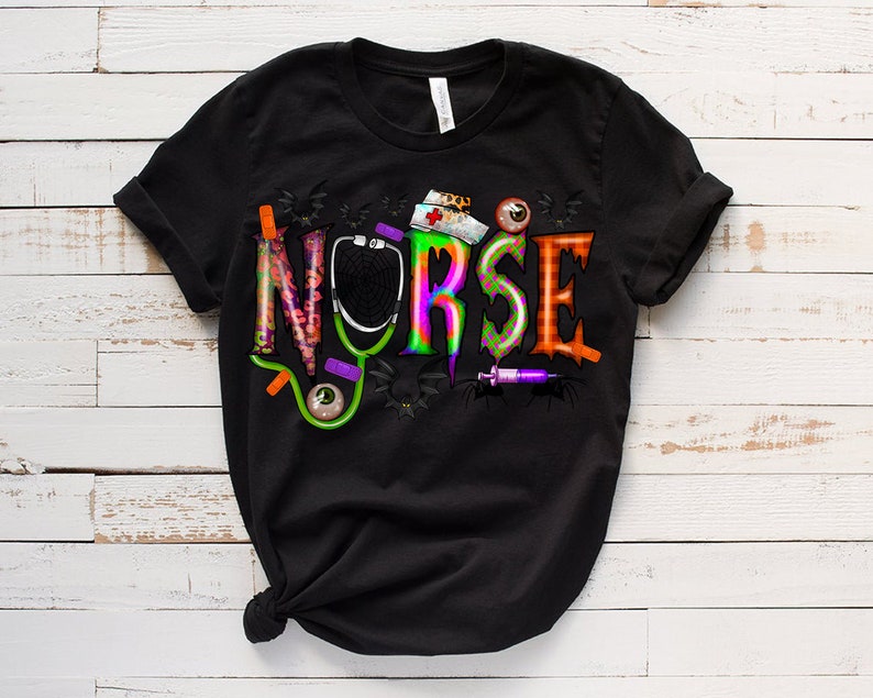 Puede incluir: Camiseta negra con un gr&aacute;fico colorido de la palabra "NURSE" con elementos de tem&aacute;tica de Halloween como un estetoscopio, murci&eacute;lagos y una jeringa.