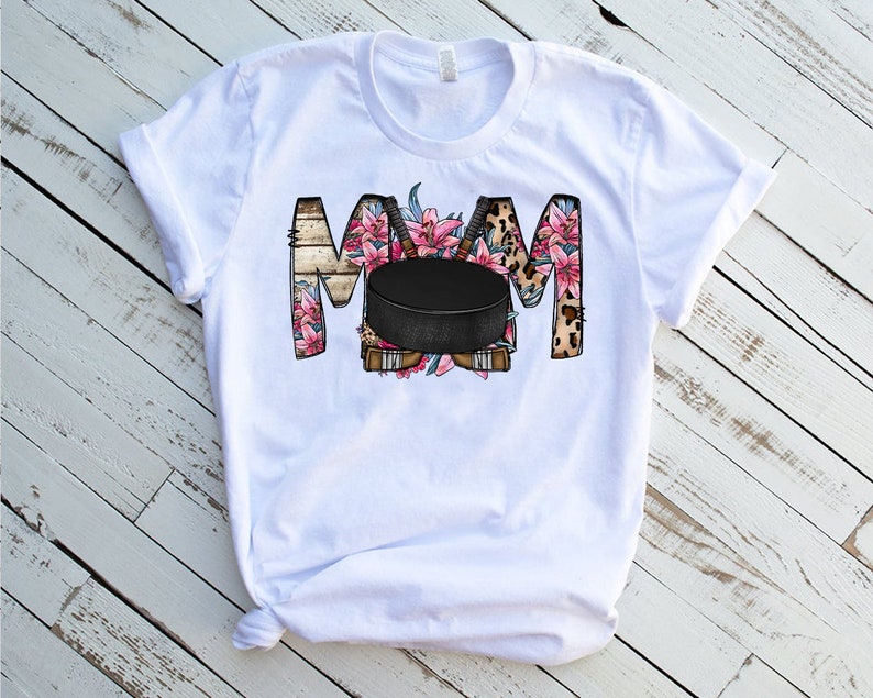 May include: White t-shirt with a floral design that spells out "MOM" with a hockey puck in the center.