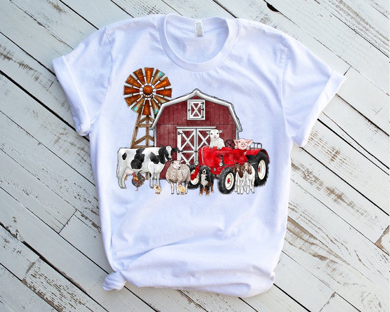 K&ouml;nnte beinhalten: Wei&szlig;es T-Shirt mit einem roten Stall, einer Windm&uuml;hle, einem roten Traktor und Nutztieren wie einer Kuh, einem Schaf, einem Schwein und einem Hund.