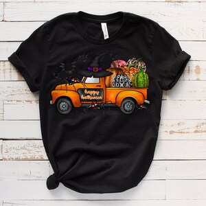 May include: A black t-shirt with a graphic of an orange pickup truck carrying pumpkins, a witch's hat, and other Halloween decorations. The truck has the words "Happy Halloween" written on the side.