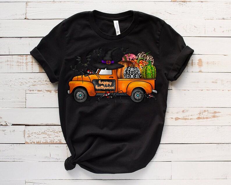 May include: A black t-shirt with a graphic of an orange pickup truck carrying pumpkins, a witch's hat, and other Halloween decorations. The truck has the words "Happy Halloween" written on the side.