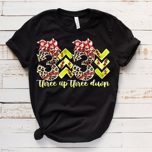 Peut inclure: T-shirt noir avec un graphique de deux num&eacute;ros de softball "3" avec un imprim&eacute; l&eacute;opard et des n&oelig;uds rouges. Le texte "Three up Three down" est sous les num&eacute;ros.