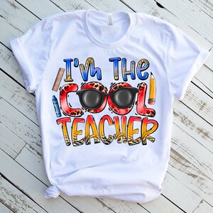 May include: White t-shirt with the text "I'm the Cool Teacher" in colorful letters with a pair of sunglasses and school supplies.
