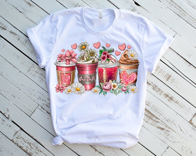May include: White t-shirt with a graphic of three coffee cups with pink and red hearts, flowers, and the word "Mama" on one of the cups.