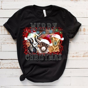 May include: Black t-shirt with a Christmas design featuring three goats wearing Santa hats and a red and black leopard print background. The text "Merry Christmas" is printed on the shirt.