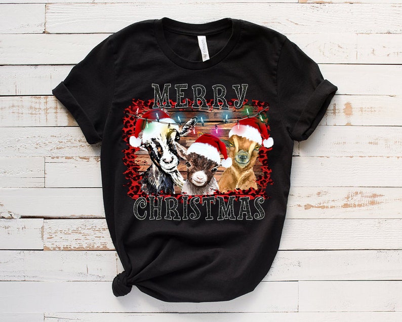 May include: Black t-shirt with a Christmas design featuring three goats wearing Santa hats and a red and black leopard print background. The text "Merry Christmas" is printed on the shirt.