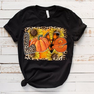 May include: Black t-shirt featuring a graphic design of the word "love" created using pumpkins, sunflowers, and leopard print.