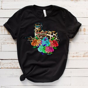 May include: Black t-shirt with a graphic of the state of Texas in leopard print with the words "Texas Strong" inside the outline. The state is surrounded by a colorful bouquet of flowers.