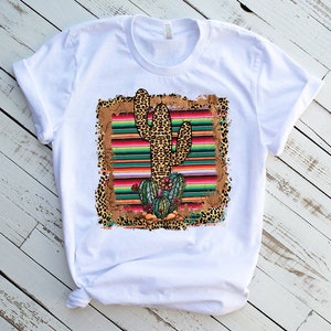 May include: White t-shirt with a graphic of a cactus in a colorful striped pattern with leopard print accents.