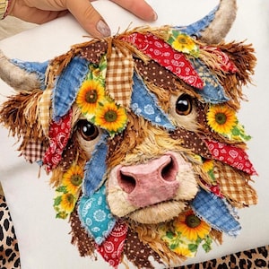 May include: A decorative pillow featuring a Highland cow design. The cow's face is crafted with various fabric scraps in shades of brown, blue, red, and yellow, with sunflower accents. The cow has large, expressive eyes and a pink nose.