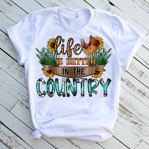 May include: White t-shirt with a graphic design that says "Life is better in the country". The graphic features a chicken, sunflowers, and a green and blue plaid pattern.