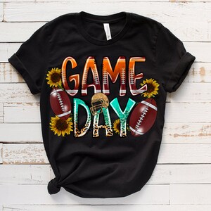 May include: Black t-shirt with a graphic design that says "Game Day" in colorful letters with footballs, sunflowers, and a football helmet.