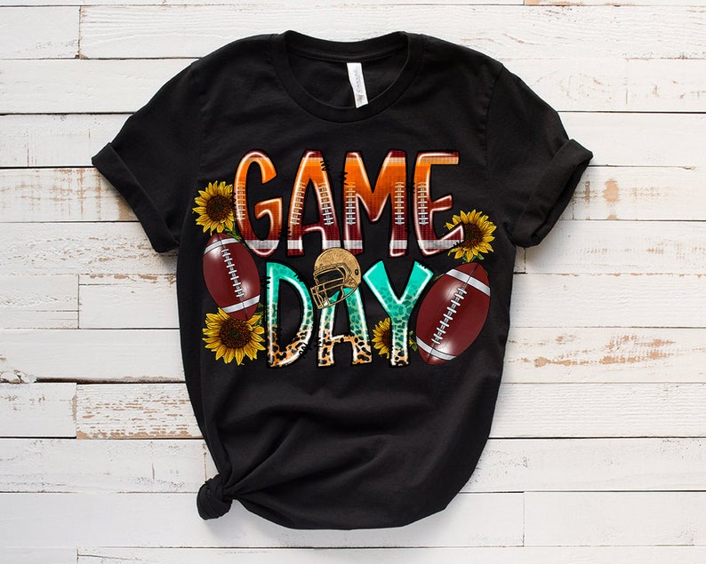 May include: Black t-shirt with a graphic design that says "Game Day" in colorful letters with footballs, sunflowers, and a football helmet.