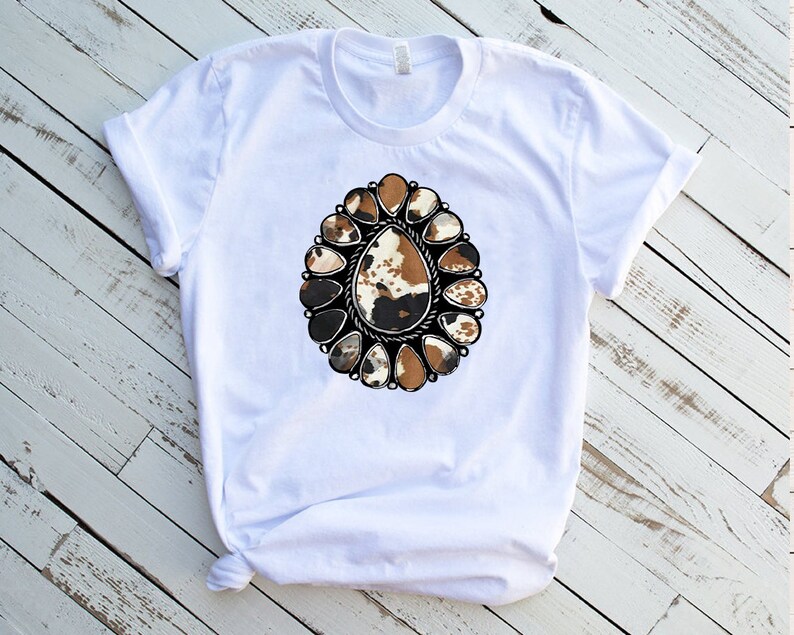 Pode incluir: Camiseta branca com um design estampado de concho prateado adornado, em couro de vaca marrom, preto e branco.