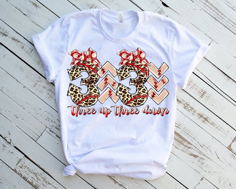 Puede incluir: Camiseta blanca con un gr&aacute;fico de dos n&uacute;meros 3 con estampado de leopardo y lazos rojos. El texto "three up three down" est&aacute; debajo de los n&uacute;meros.