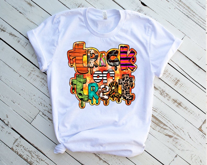 May include: White t-shirt with a colorful "Trick or Treat" graphic design. The design features a variety of patterns and textures, including stripes, leopard print, and animal print.