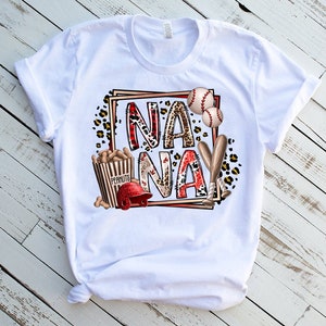 May include: White t-shirt with a graphic design featuring the word "NANAY" in red and black letters with a baseball theme. The design includes baseball bats, baseballs, peanuts, and a baseball cap.
