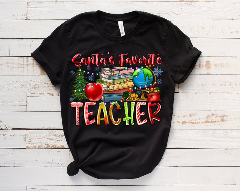 Puede incluir: Una camiseta negra de manga corta con el texto Santa's Favorite TEACHER en letras rojas y multicolores. El gr&aacute;fico incluye una pila de libros, un globo terr&aacute;queo, una manzana roja, un &aacute;rbol de Navidad y luces con copos de nieve.