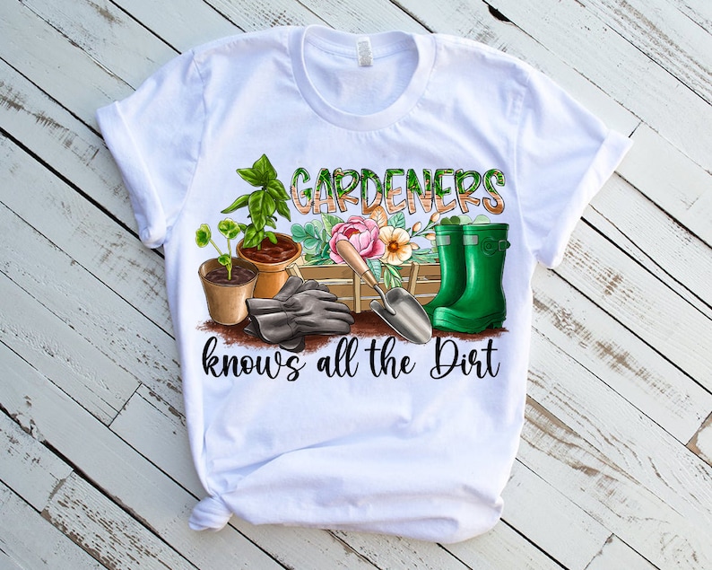 May include: White t-shirt featuring a green, brown, and pink gardening themed graphic. The graphic includes gardening gloves, a trowel, a watering can, and potted plants. The text on the shirt reads "Gardeners know's all the dirt".