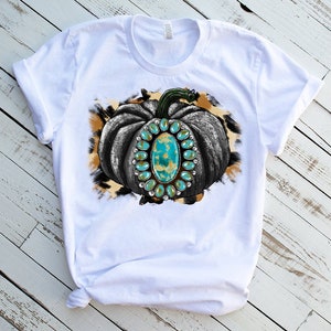 Puede incluir: Camiseta blanca con un gr&aacute;fico de una calabaza en blanco y negro con piedras preciosas turquesa sobre un fondo de estampado de leopardo marr&oacute;n y blanco.