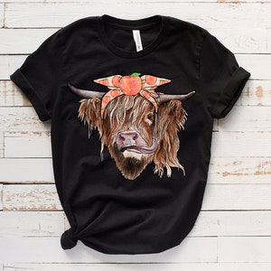 Op de afbeelding: Zwart T-shirt met een afbeelding van een Schotse hooglander die een perzikkleurig bandana draagt met perzikplakjes.