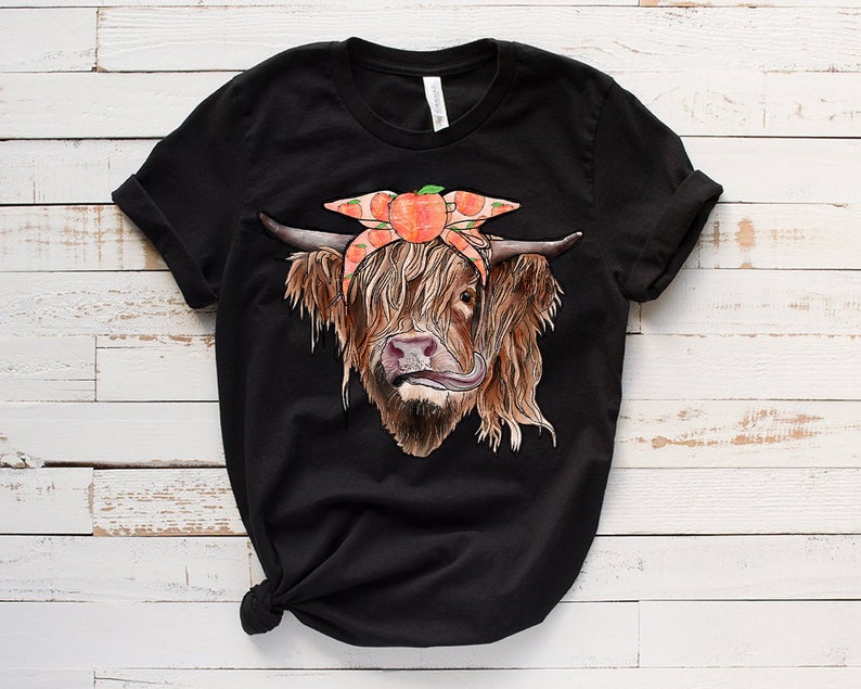 Op de afbeelding: Zwart T-shirt met een afbeelding van een Schotse hooglander die een perzikkleurig bandana draagt met perzikplakjes.