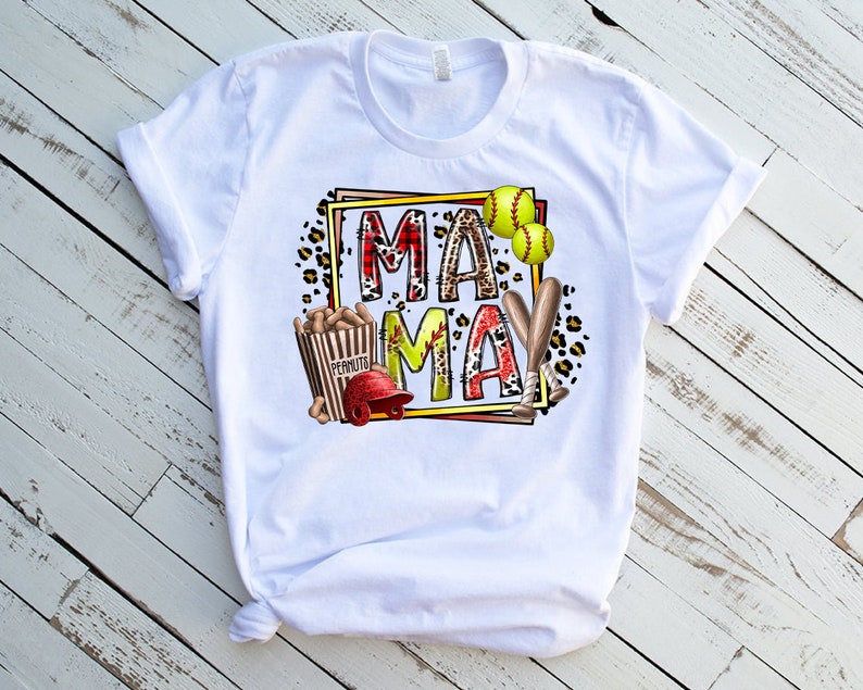 May include: White t-shirt with a graphic design featuring the words "Mama May" in a colorful, patterned frame. The design also includes baseballs, bats, and a bag of peanuts.