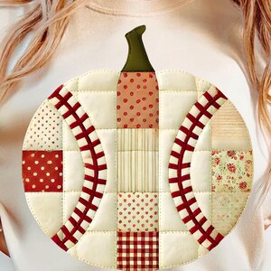 Puede incluir: Un diseño de calabaza acolchada con un tallo verde y una variedad de parches de tela rojos y crema. La calabaza está hecha de cuadrados y secciones curvas, con lunares, rayas y patrones de cuadros. El diseño está en una camiseta blanca.