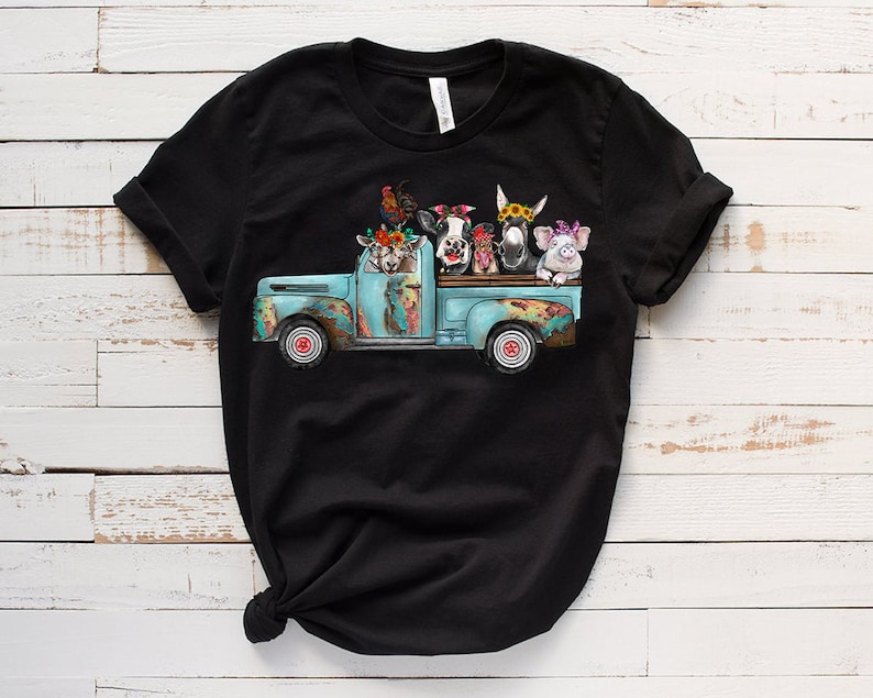 May include: A black t-shirt featuring a graphic of a blue pickup truck carrying a variety of farm animals, including a cow, pig, donkey, goat, and rooster. The animals are wearing flowers and are looking out of the truck bed.