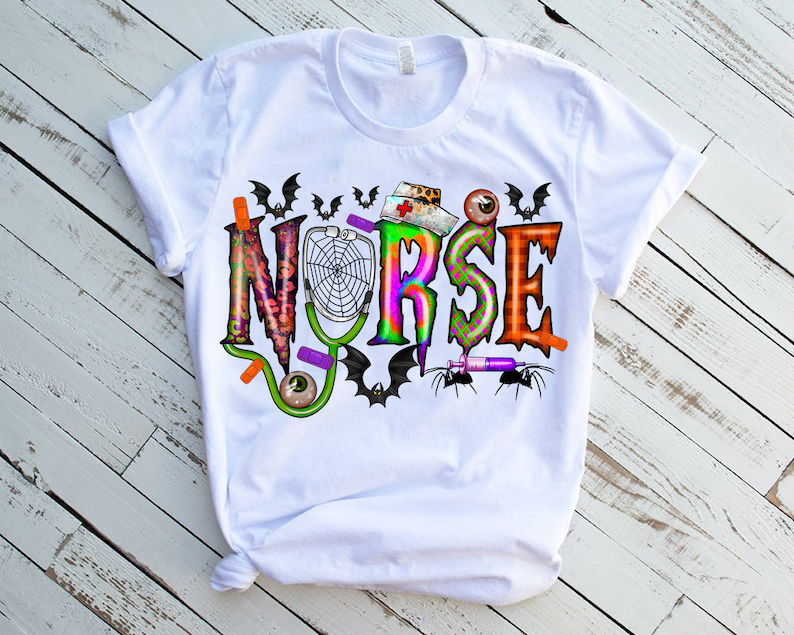 Puede incluir: Camiseta blanca con un dise&ntilde;o gr&aacute;fico colorido que dice "NURSE" con im&aacute;genes de tem&aacute;tica de Halloween como murci&eacute;lagos, ara&ntilde;as y una telara&ntilde;a.