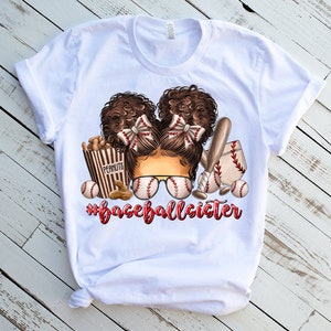 Peut inclure: T-shirt blanc avec un motif repr&eacute;sentant une fille aux cheveux bruns portant des lunettes de soleil de baseball et un n&oelig;ud rouge. Le motif comprend &eacute;galement des balles de baseball, une batte et une bo&icirc;te de cacahu&egrave;tes. Le texte "#baseballsister" est imprim&eacute; sous le motif.
