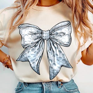 May include: A white t-shirt with a large silver bow printed on the front. The bow is made of bubble wrap material.