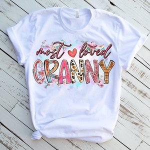 May include: White t-shirt with a pink, red, and brown graphic that says "most loved granny" with a heart and floral accents.
