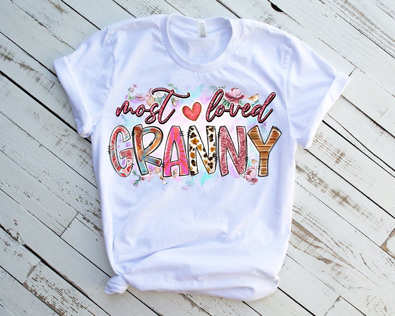 May include: White t-shirt with a pink, red, and brown graphic that says "most loved granny" with a heart and floral accents.