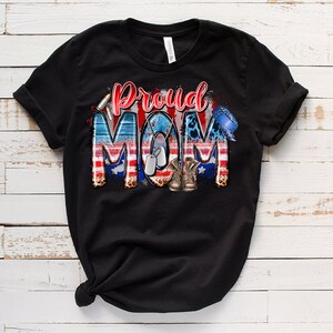 Może przedstawiać: Czarny T-shirt z nadrukiem graficznym sł&oacute;w "Proud Mom" w kolorze czerwonym, białym i niebieskim z wzorem amerykańskiej flagi, wojskowymi identyfikatorami i butami.
