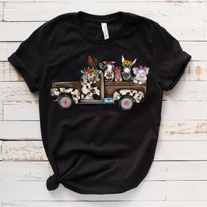May include: Black t-shirt with a graphic of a vintage pickup truck filled with farm animals wearing flower crowns. The animals include a cow, a goat, a donkey, a pig, and a rooster.