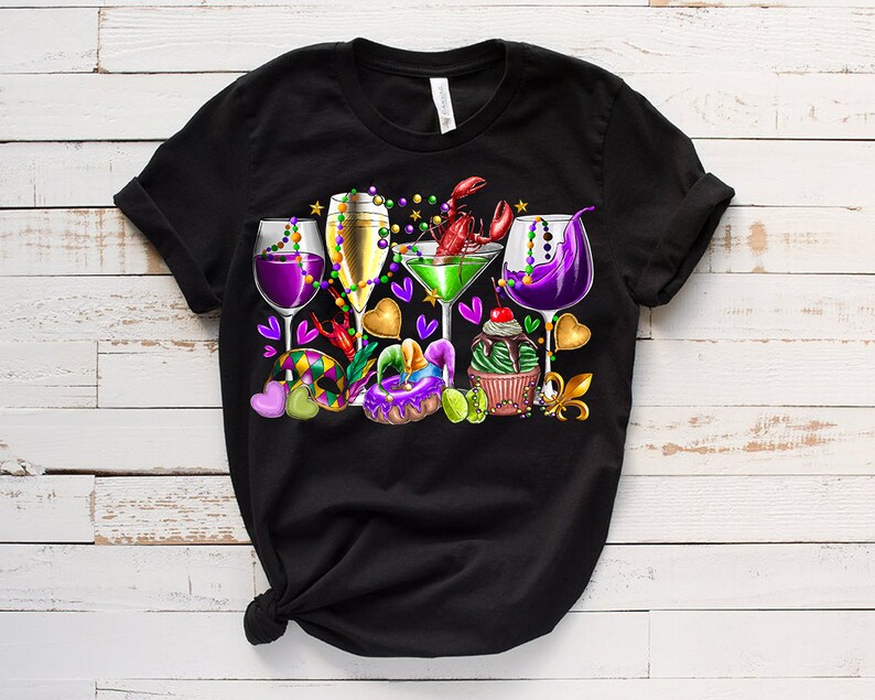 May include: Black t-shirt with a colorful Mardi Gras design featuring glasses of wine, a cocktail, beads, a cupcake, a donut, and a crawfish.