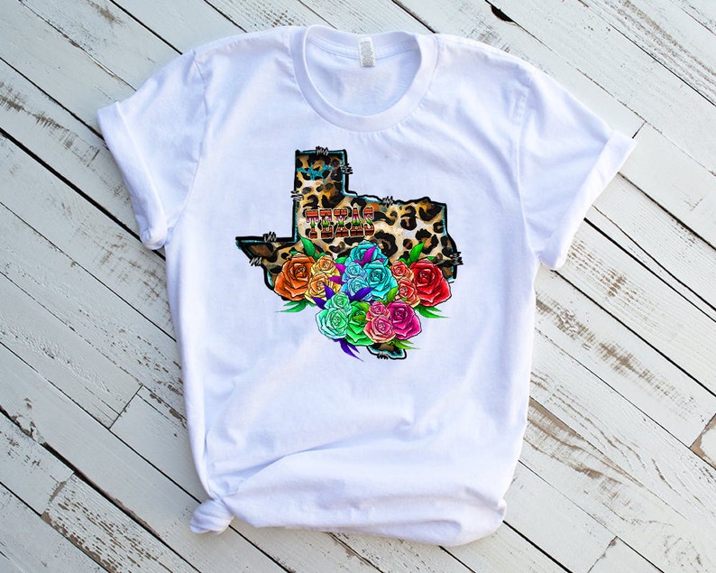 May include: White t-shirt with a graphic of the state of Texas in a leopard print with colorful flowers around it. The text "Texas Tough" is inside the state outline.