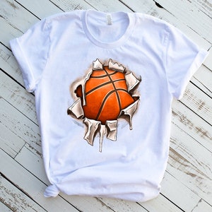 Peut inclure: T-shirt blanc avec un motif de ballon de basket qui &eacute;clate &agrave; travers le tissu. Le ballon de basket est orange et marron.