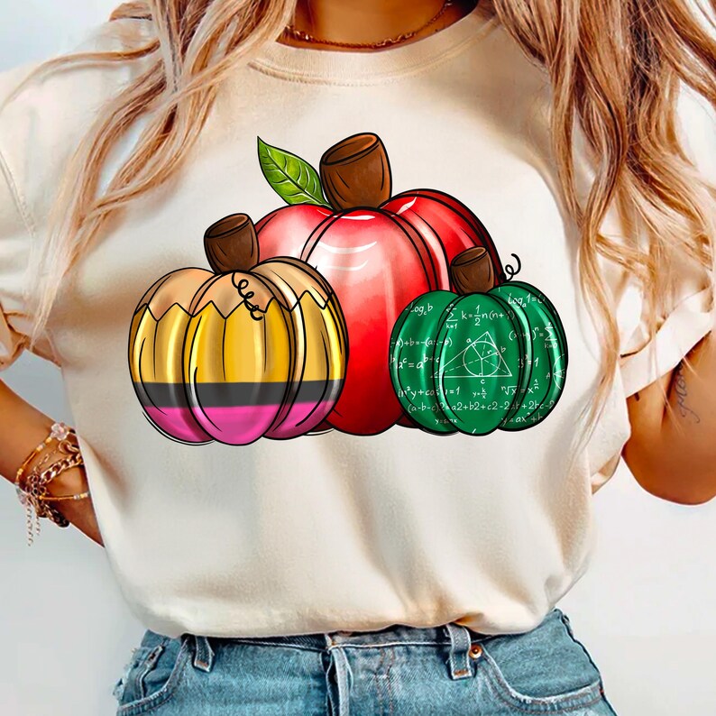 May include: A white t-shirt with a graphic of three pumpkins. The pumpkins are decorated with math equations and a pencil. The pumpkins are red, green, and yellow.