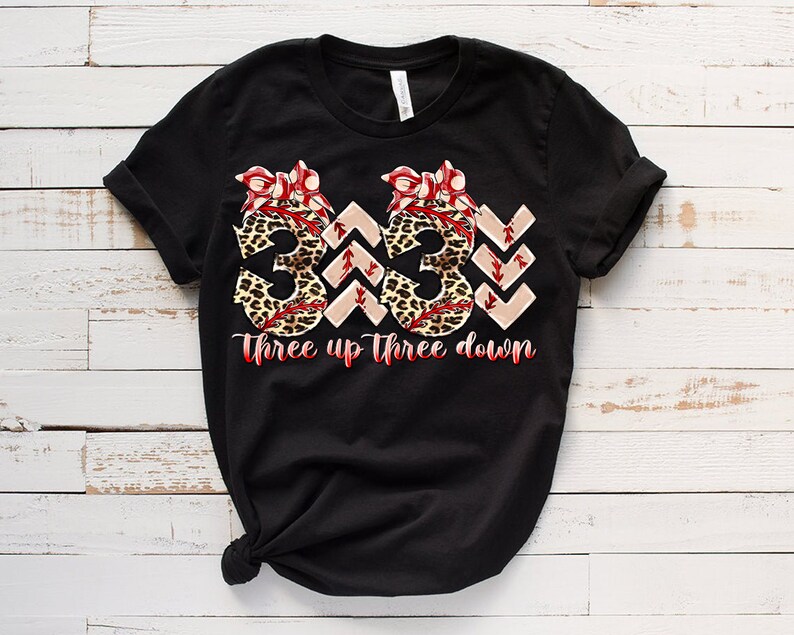 Puede incluir: Camiseta negra con un gr&aacute;fico de tres pelotas de b&eacute;isbol con estampado de leopardo y lazos rojos. El texto "Three up Three down" est&aacute; impreso debajo de las pelotas de b&eacute;isbol.