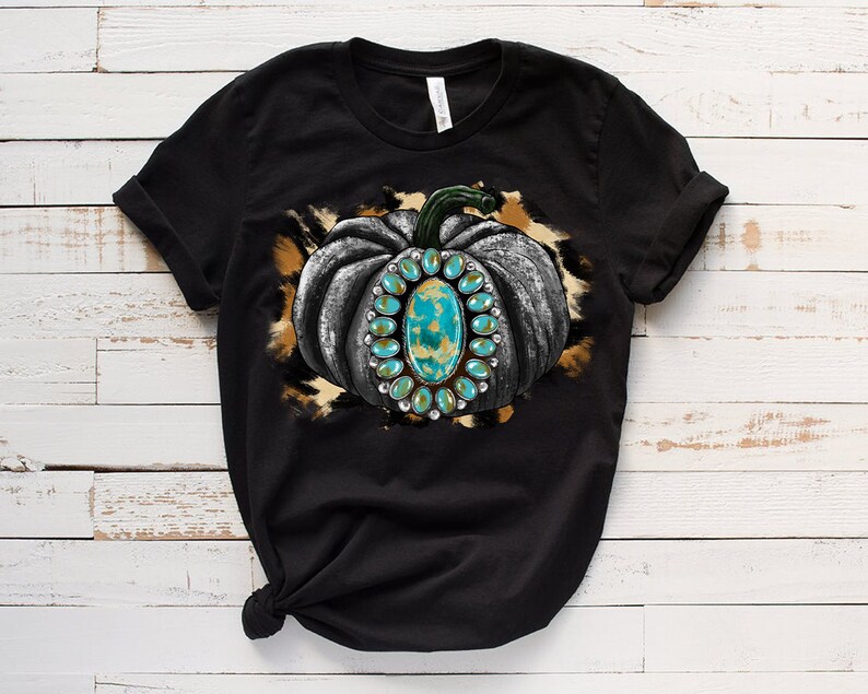 Puede incluir: Camiseta negra con un gr&aacute;fico de una calabaza gris con detalles turquesa y dorados sobre un fondo de estampado de leopardo marr&oacute;n y blanco.