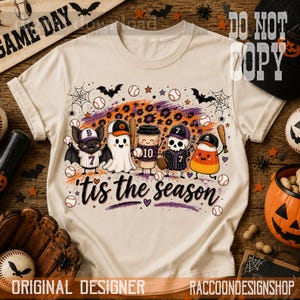May include: A cream-colored t-shirt featuring a graphic print of a bat, ghost, coffee cup, skeleton, and candy corn wearing baseball caps and holding bats. The design includes baseballs, spiderwebs, and the text 'tis the season' in black.