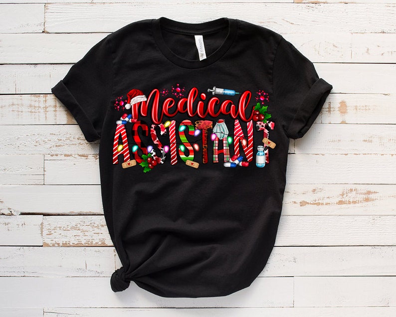 Puede incluir: Camiseta negra con un dise&ntilde;o navide&ntilde;o rojo y blanco que dice "Asistente M&eacute;dico". El dise&ntilde;o incluye bastones de caramelo, vendas y otros s&iacute;mbolos m&eacute;dicos.