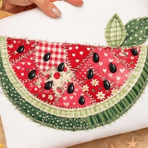 Puede incluir: Un artículo de tela blanca con un diseño de rodaja de sandía en patchwork. La sandía tiene tela roja con corazones blancos, flores y un patrón de cuadros. Semillas negras y corteza verde completan el diseño. Se adjuntan dos hojas verdes.