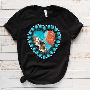 以下が含まれることがあります： ターコイズとブラウンのハート型のデザインが施された黒いTシャツ。ハートはターコイズビーズの円に囲まれています。