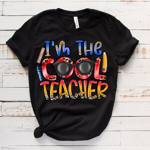 May include: Black t-shirt with the text "I'm the Cool Teacher" in colorful letters with a pair of sunglasses and school supplies.